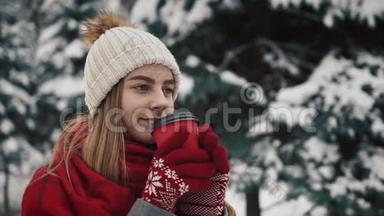 年轻漂亮的女孩穿着暖和的衣服<strong>站在雪中</strong>的圣诞树旁边，从纸杯里喝咖啡